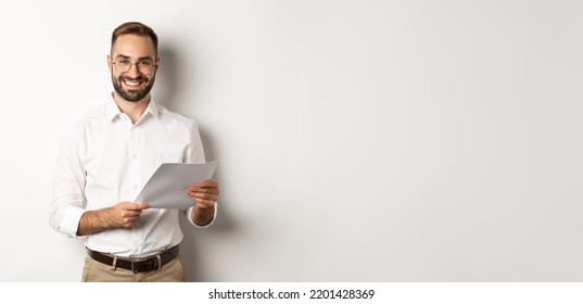 Employer looking satisfied with work, reading documents and smiling pleased, standing over white background - Shutterstock ID 2201428369