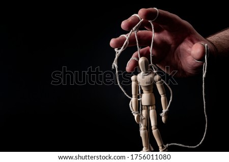 Employer manipulating the employee, emotional manipulation and obey the master concept with ominous hand pulling the strings on a marionette with moody contrast on black background with copy space