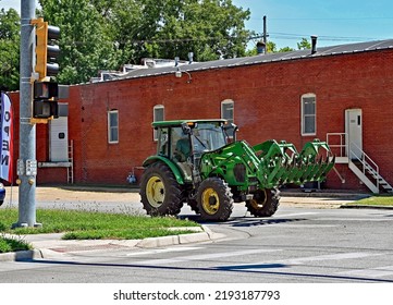 EMPORIA, KANSAS, USA - AUGUST 13, 2022
John Deere Tractor With Hay Bale Attachment Drives Driving On Main Street From One Farm To Another To Finish Stacking Hay Bales
