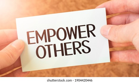 Empower Others Word Inscription On White Card Paper Sheet In Hands Of A Businessman. Recap Concept. Red And White Paper