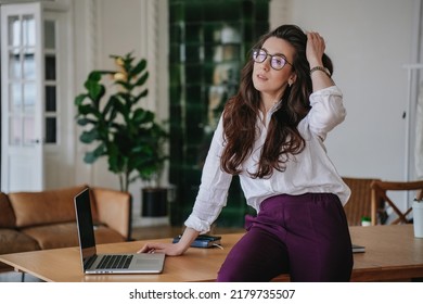 Empowered Hispanic Brunette Woman In Glasses With Wavy Loose Hair In White Shirt Looking Aside Confidently Over Blurry Office. Portrait Of Smart Student At Home. Business And Education