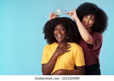 Empowered Women, Empower Women. Studio Shot Of A Young Woman Putting A Crown On Her Friend Against A Blue Background.