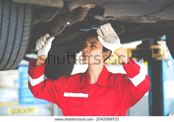 Empowering caucasian waman\
mechanic wearing red uniform working Under a Vehicle in a Car\
Service station. Expertise mechanic working in automobile repair\
garage.