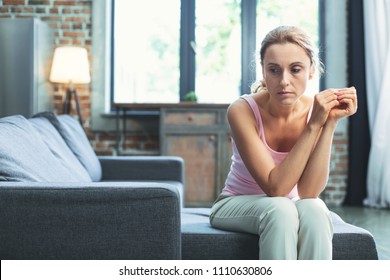 Emptiness In Heart. Sad Mature Woman Gazing Aside And Seating On Couch