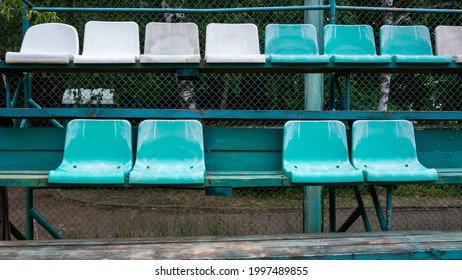 Empty 2 rows of simple
green, white plastic chairs attached to wooden bleachers to watch sport game. One is missing.