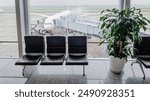 Empty airport waiting area with seats and potted plant, featuring a parked airplane at the gate, representing travel delays