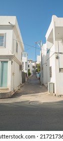 Empty Alley Way In A Rural Tourist Town Surrounded By White Houses Or Apartments. A Narrow City Street In Europe. A Quiet Road In An Urban Village Area. Hidden Side Street With Modern Architecture