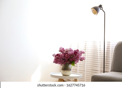 Empty apartment with minimal loft style interior, wooden floor and glass vase with bouquet of lilacs on foreground and blank wall with a lot of copy space for text on background. Close up.