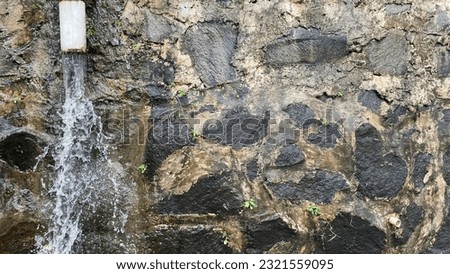 The empty area of the black river stone wall was wet from the rain with water pouring out of the pipe