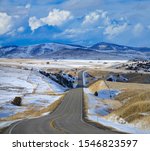 Empty asphalt freeway runs across the beautiful snowy Montana countryside in early spring. Scenic vista of an interstate highway crossing the gorgeous rural landscape under the Rocky Mountains.