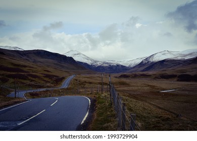 An empty asphalt mountain road leading to the snow capped mountain peaks of Cairngorms National Park, Highland Scotland. No vehicles, wild nature and freedom