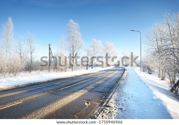 An empty asphalt road after cleaning.
Street lanterns close-up. Car tracks in a fresh snow. Snow-covered
birch forest in the background. Clear blue sky. Winter driving in
Finland. Global warming
theme
