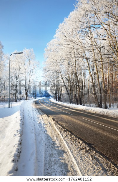 An empty asphalt road after cleaning.\
Street lanterns close-up. Car tracks in a fresh snow. Snow-covered\
birch forest in the background. Clear blue sky. Winter driving in\
Finland. Global warming\
theme