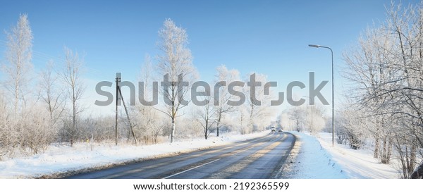 An empty asphalt road after cleaning.\
Street lanterns close-up. Car tracks in a fresh snow. Snow-covered\
birch forest in the background. Clear blue sky. Winter driving in\
Finland. Global warming\
theme