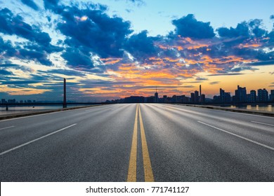 Empty Asphalt Road And City Skyline At Sunset