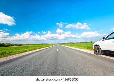 Empty asphalt Road in fields toward to the blue sky with white car standing on wayside. Colorful summertime outdoors horizontal image with perspective. - Shutterstock ID 426953005