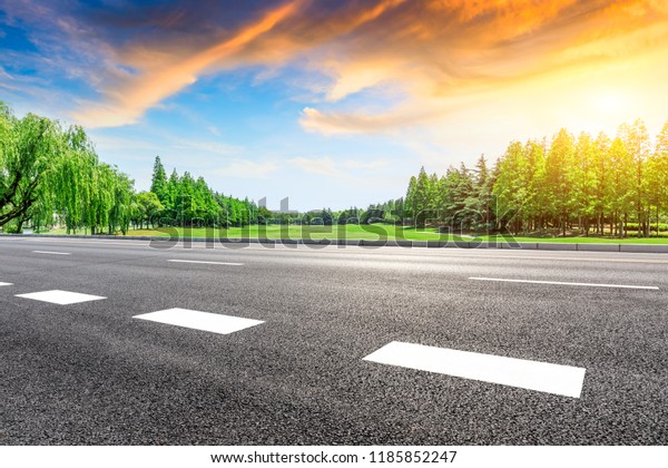 Empty asphalt road and green forest with colorful\
clouds at sunset