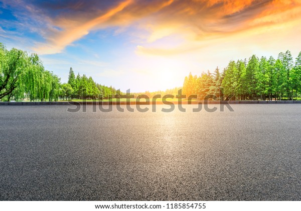 Empty asphalt road and green forest with colorful\
clouds at sunset