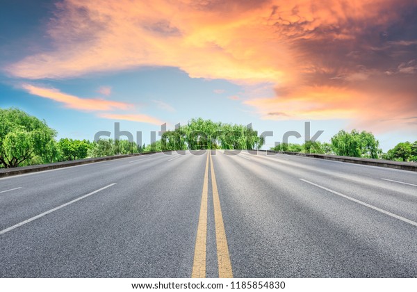 Empty asphalt road and green forest with colorful
clouds at sunset