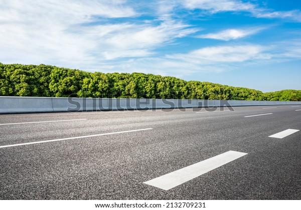 Empty asphalt road and green forest under\
blue sky. Road and forest\
background.