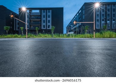 Empty asphalt road at an intersection with traffic lights between modern factory at dusk.