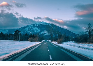 Empty asphalt road leads towards a majestic snow capped mountain in slovakia, under a dramatic sunset sky with pink and purple hues. Slovakia Route 66. - Powered by Shutterstock