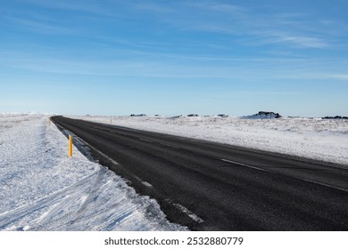 Empty asphalt road, no cars or traffic in an Icelandic volcanic landscape. Day time, sunny weather, snowy road and landscape. Remote wilderness, big distance, road trip during winter. - Powered by Shutterstock