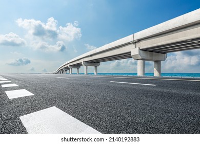 Empty asphalt road and river with bridge under blue sky