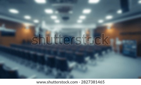 An empty auditorium hall with many rows of dark seats facing a stage area with bright overhead lighting.