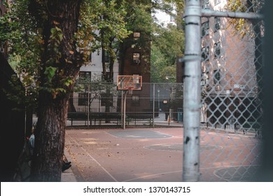 Empty basketball court and net surrounded by fences and trees in Lower Manhattan, New York