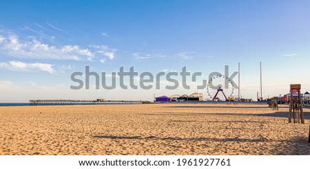 Empty beach of the popular tourist destination, Ocean City, Maryland. Image shows an afternoon view of the pier, board walk, shops, ferris wheel, lifeguard stands and the ocean at distance.