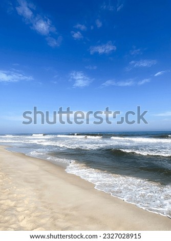 Empty beach, waves, sand, blue sky with wispy clouds on a summer day. Bright, hazy mood. Long Island, New York State, Atlantic Ocean. Vertical.