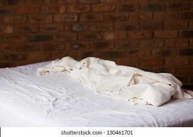 Empty bed and white sheet and cover with a brown brick wall in the background