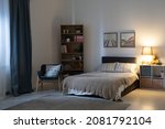 Empty bedroom with electric lamp on shelves, cozy armchair, pictures above bed at night