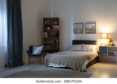 Empty bedroom with electric lamp on shelves, cozy armchair, pictures above bed at night - Shutterstock ID 2081792104