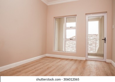 An Empty Bedroom Of A Newly Build House With Laminated Floor And Glass Windows And Door That Lead Out To The Patio.