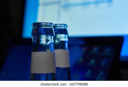 Empty Beer Bottles, Upper Part, In Front Of A Switched On Computer. Selective Focus. Concept For Alcohol Abuse And Alcohol Dependency At The Workplace