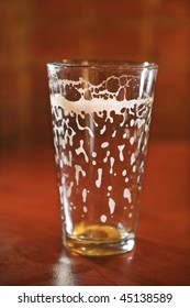 Empty beer glass on bar counter with residual foam lining the glass. Vertical shot.