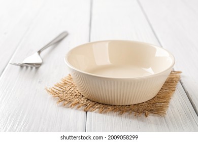 Empty Beige Bowl And Metal Fork On A White Wooden Table. Clean Porcelain Soup Bowl On A Table. Empty Ceramic Tableware Ramekin For Food Design Mockup. High Key Image. Front View.