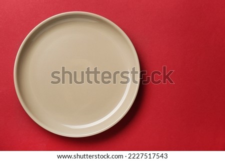 Empty beige ceramic plate on red background, top view. Space for text