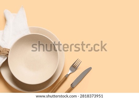 Empty beige ceramic plates with a white napkin and cutlery on a peach background, top view with copy space, this top-view composition provides ample copy space for various design and advertising needs