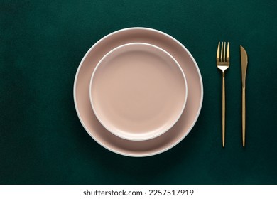 Empty beige plate, golden fork and knife on a dark green background. Top view, copy space. Table setting. Flat design - Powered by Shutterstock