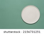 Empty beige plate on green pastel paper background. Top view, flat lay. Textured object, selective focus.