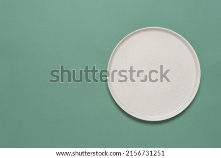 Empty beige plate on green pastel paper background. Top view, flat lay. Textured object, selective focus.