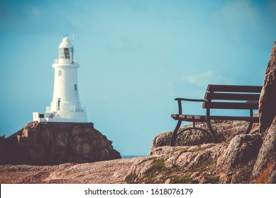 An empty bench by the coastline overlooking La Corbiere Lighthouse in Jersey