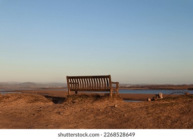 Empty bench on a beach overlooking countryside landscape with sand and no people overlooking river and beautiful peaceful scenery with a shore and sandy landscape