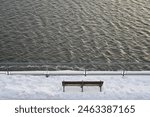 Empty bench on a snowy platform overlooking the Saint Lawrence river in Montreal.