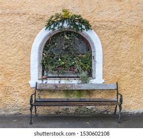 Empty bench under a decorated window of a historic house.