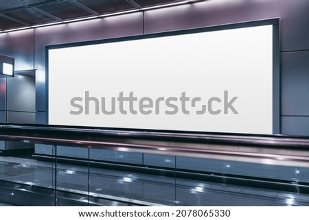 An empty billboard mockup next to a travelator in a modern airport arrival area; a white blank poster template indoors of a terminal of public transport building or shopping mall near a moving walkway