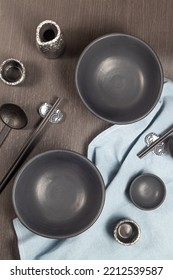 An Empty Black Bowl Complete With A Sake Glass Is Placed On A Black Wooden Table And A Blue Tablecloth